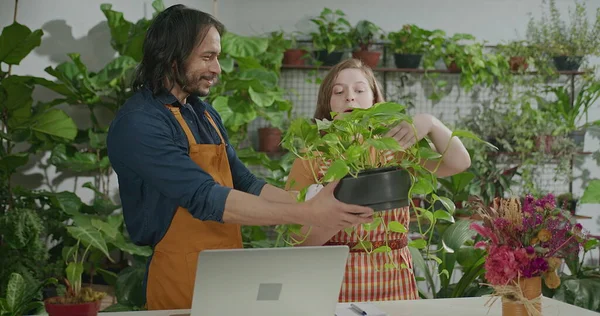 Young entrepreneurs managing online orders at small business flower shop. Male a female employee staff wearing apron writing notes using internet to expand business