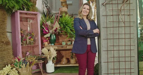 Portrait of female business owner of local flower shop standing in storefront smiling at camera with arms crossed. Happy entrepreneur of local small business flower store