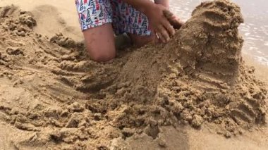 Young boy playing with sand at the beach, making mountain