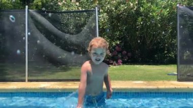 Toddler baby boy at swimming pool splashing water to camera