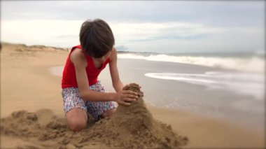 Young boy playing with sand at the beach, making mountain