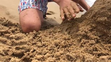 Young boy playing with sand at the beach, making mountain