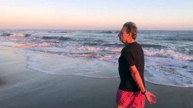 Person walking at the beach during sunset, contemplative and thoughtful senior man