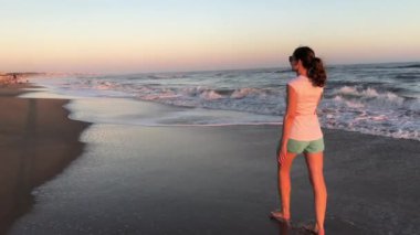 Woman walks at the beach shore during sunset
