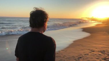 Older retired man walking at the beach shore during sunset