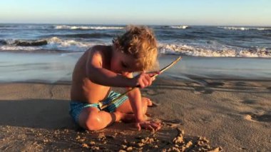 Toddler baby boy playing at the beach with stick