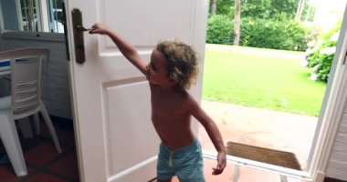 Toddler boy closing front door behind him, leaving house, reaching door knob