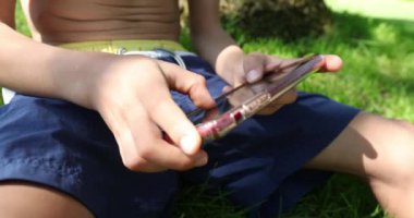 Close-up of child hands holding cellphone touching screen outdoors