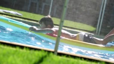 Kid playing at the swimming pool, on top of inflatable mattress