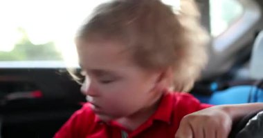 Toddler boy shaking head in the backseat of a car, scratching face