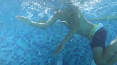 Çocuk havuzda yüzüyor, genç bir çocuğun suları altında.