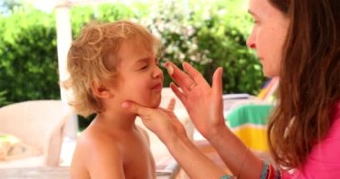 Anne erkek bebeğe güneş kremi sürüyor.