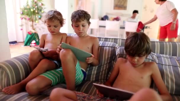 家里沙发上的孩子们在智能手机和平板电脑上玩电子游戏 — 图库视频影像