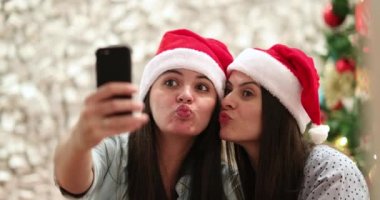Kız kardeşler Noel Baba şapkası takıp selfie çekiyorlar. Tatillerde akıllı telefonla fotoğraf çeken bayan arkadaşlar.