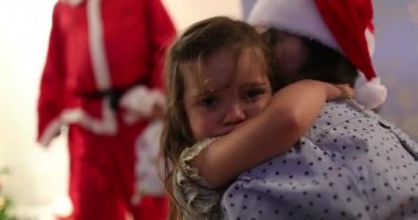 Yorgun küçük kız evde Noel Baba 'ya bakıyor annesine sarılıyor utangaç hissediyor.