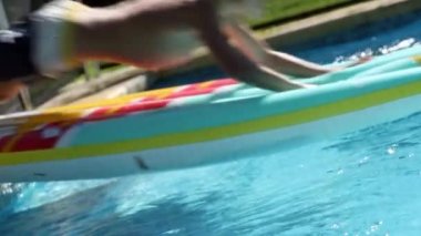Child jumping on top of inflatable mattress, sliding into swimming pool water
