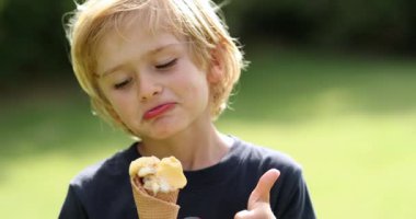 Sarışın küçük çocuk dondurma yiyor ve baş parmağını bırakıyor.