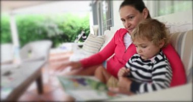 Casual real life moment of mother telling reading story book to her child boy