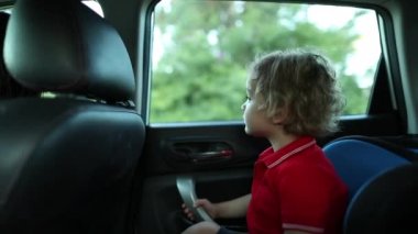 Toddler looking out car window. Baby seated in car backseat