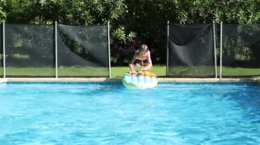 Young boy kid jumping on top of inflatable mattress, having fun at the pool