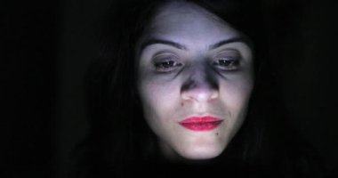 Woman face looking at cellphone screen in pitch blackness, blue screen glow