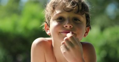 Little boy outside eating cookie laid on grass happy