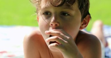 Portrait of little boy eating cookie laid on grass