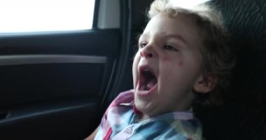 Passenger little boy yawning while in the back seat of a car traveling, candid and casual