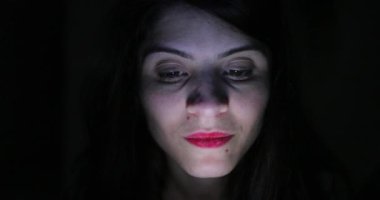 Woman face looking at blue light screen. Person using cellphone at night in the dark