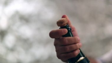 Closeup of hand holding champagne bottle opening in slow-motion