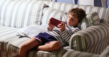 Child playing video-game on cellphone device at home seated on sofa, candid