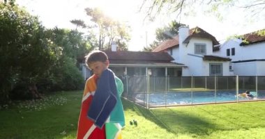 Home swimming pool setting, little boy covered in towel after playing in the water, sunlight flare