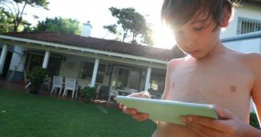 Little boy using tablet device technology in backyard home with sunlight lens-flare
