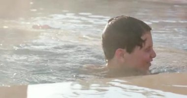 Yüzme havuzunda oynayan çocuk, küçük çocuğa su sıçratıyor.