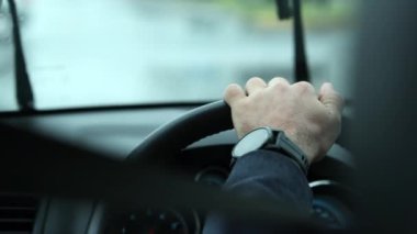 Closeup of hand holding steering wheel waiting in red light during rainy day