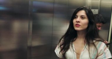 30 'larında bir kadın asansör aynasının önünde kendini kontrol ediyor ve kapıları açıyor.