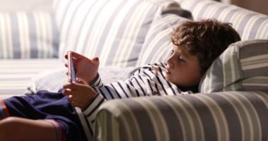 Koltukta elinde teknoloji cep telefonu olan genç bir çocuk video oyunu oynuyor.