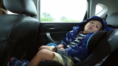 Little boy sticking tongue out while in the backseat of a car on the road