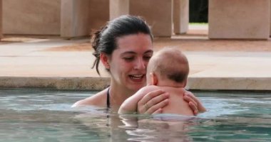 Casual happy young mother holding newborn baby infant son inside water