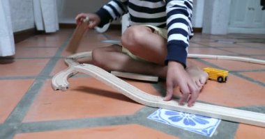 Child playing with traditional wooden car roads. Toddler boy plays connecting road pieces together