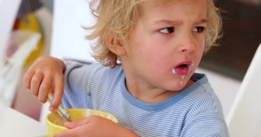 Candid real life cute child complaining while eating yogurt for breakfast, adorable baby boy doing funny face thinking