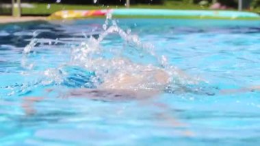 Young boy going underwater at the swimming pool water and re-emerging into water surface