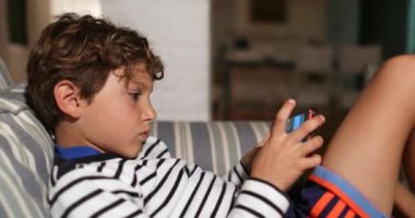 Child boy holding cellphone device playing video-game at home
