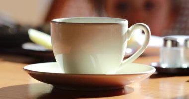Warm cup of coffee with steam with child in the background, morning breakfast scene