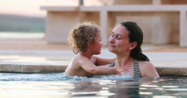 Küçük çocuk yüzme havuzunda annesine sarılıyor. Bebecik annesini kucaklıyor.
