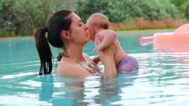 Mom holding newborn baby inside swimming pool water