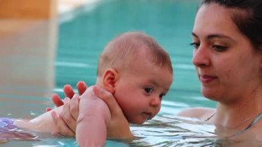 Mom holding newborn baby inside swimming pool water