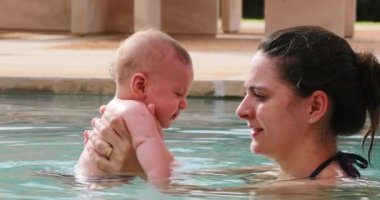 Mother and baby together at the swimming pool water, candid interaction infant and mom