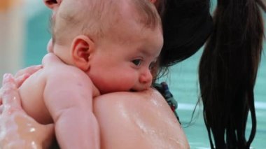 Mom holding baby boy inside swimming pool water