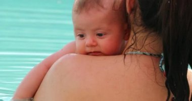 Mother holding baby at the swimming pool, kissing baby showing love and affection